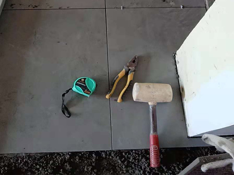 客厅地砖铺贴：铺贴的工具包括橡胶锤和粘结剂。在进行施工之前先把所需要的这些材料都整理好放在一旁备用；基层的处理工作对瓷砖的平整度有很大的影响，对于基层要做好清洁工作，还有找平工作。放样：在进行瓷砖的铺贴工作之前还事先找好垂直线，这样可以在铺贴的时候找到瓷砖的水平线，让瓷砖铺贴的更加的平整。粘结剂加水搅拌均匀，静置10分钟之后就可以使用。将瓷砖表面的浮灰清除，再在瓷砖背面均匀的涂抹上粘结剂，按照预铺的顺序将瓷砖铺贴在地面上，最后用橡胶锤轻轻拍打至服帖齐整。
